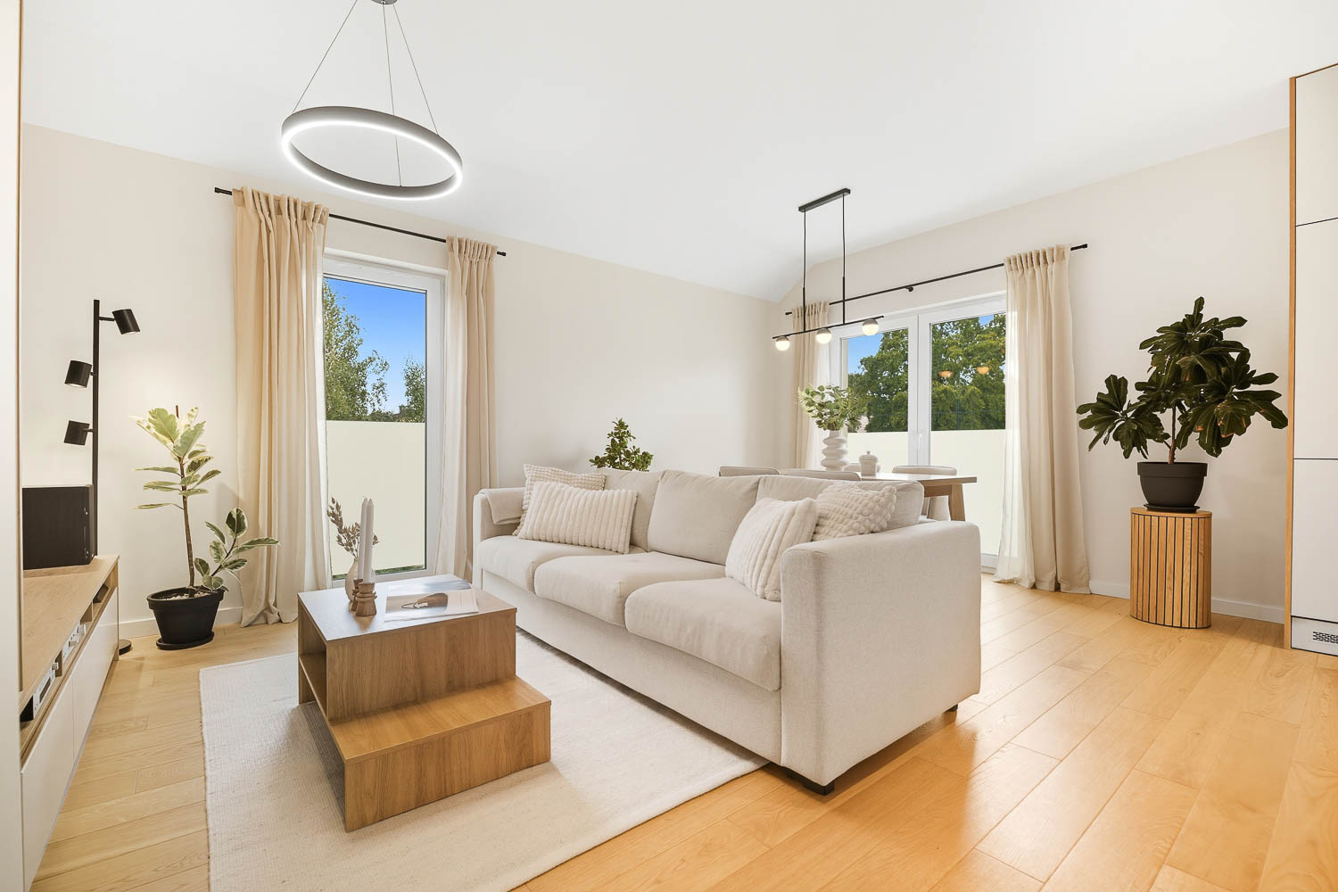 Przytulny, jasny salon z beżową sofą i drewnianym stolikiem kawowym autorstwa Grafoto. Estetyczne wnętrze z dużą ilością naturalnego światła, roślinami i minimalistycznymi dodatkam