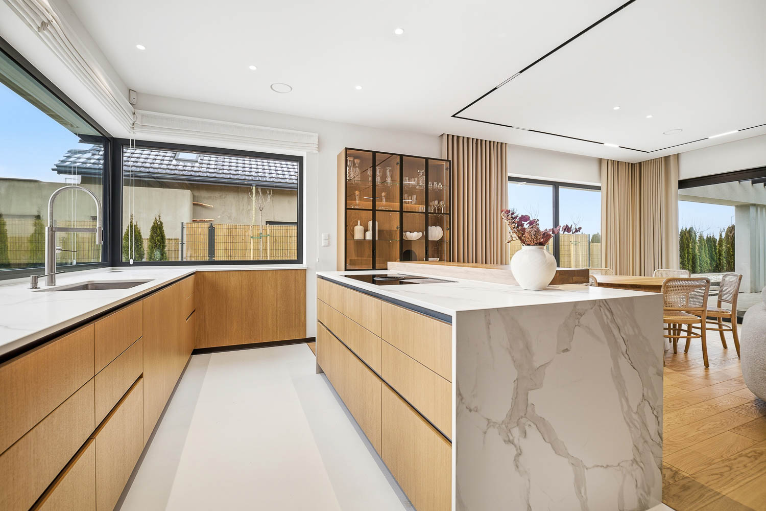 Jasna kuchnia z drewnianymi frontami, marmurową wyspą i przeszkloną witryną sfotografowana przez Grafoto.