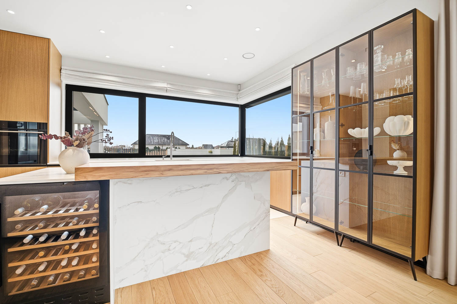 Nowoczesna kuchnia z widokiem na ogród, marmurową wyspą i drewnianą zabudową – realizacja Grafoto.