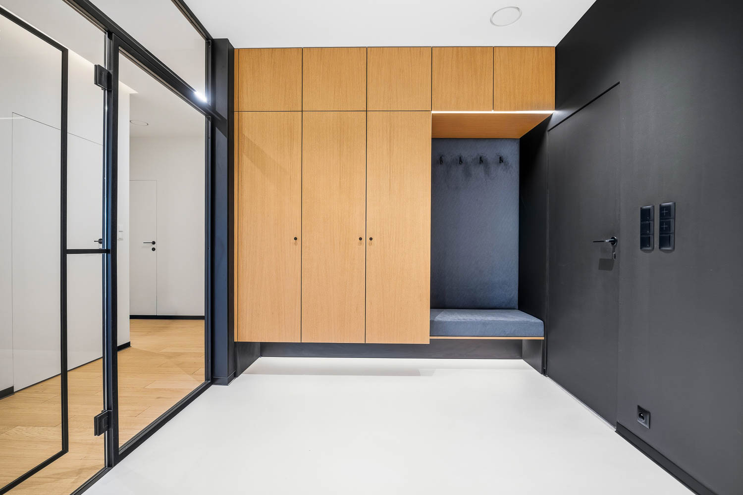 Nowoczesny wiatrołap z dębową szafą, siedziskiem i czarnymi detalami, widok na loftowe przeszklenia – realizacja Grafoto.